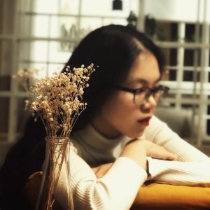 một bình hoa có nền là một cô gái tóc dài đeo kính đang trầm tư